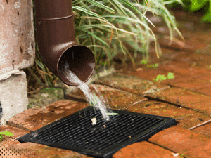 Gutter downspout draining water into ground drain in Arlington, TX during home inspection.
