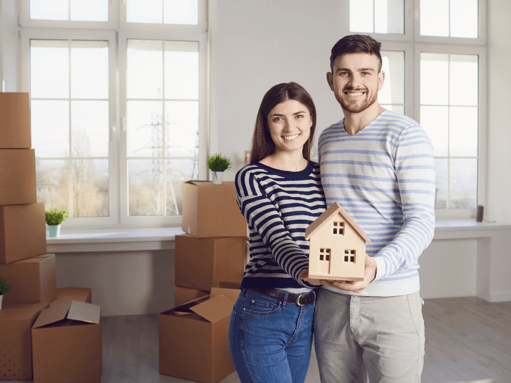 Happy homebuyers holding a model house inside their new Arlington TX property after completing a sewer scope inspection and full home inspection